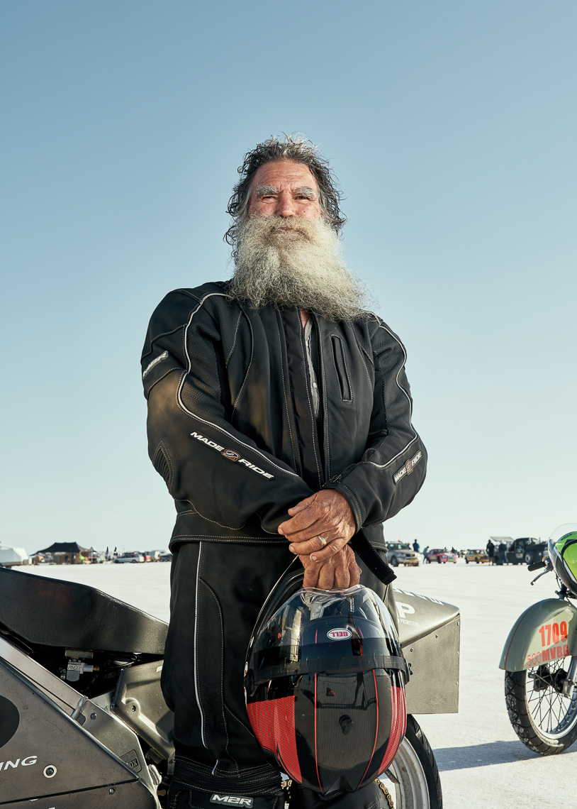 A man stands in front of a motorbike holding his helmet