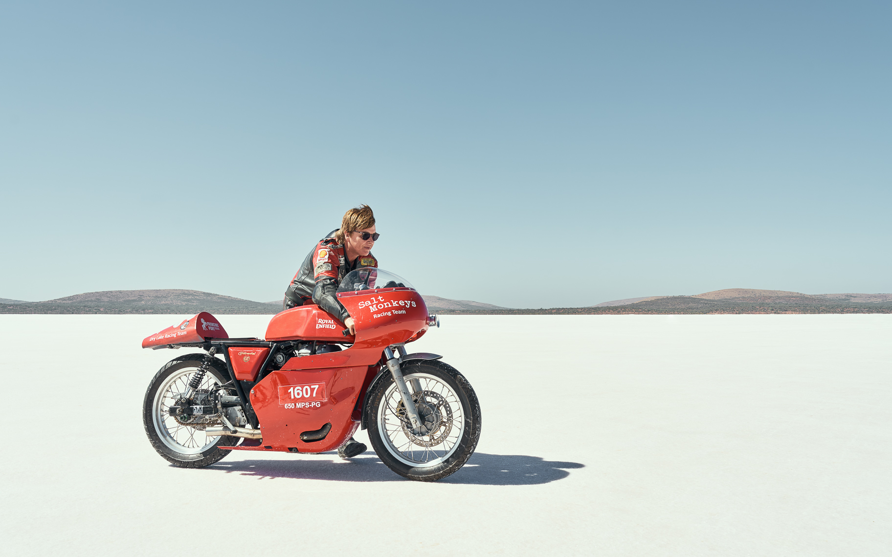A woman pushing a red motorcycle on a salt lake