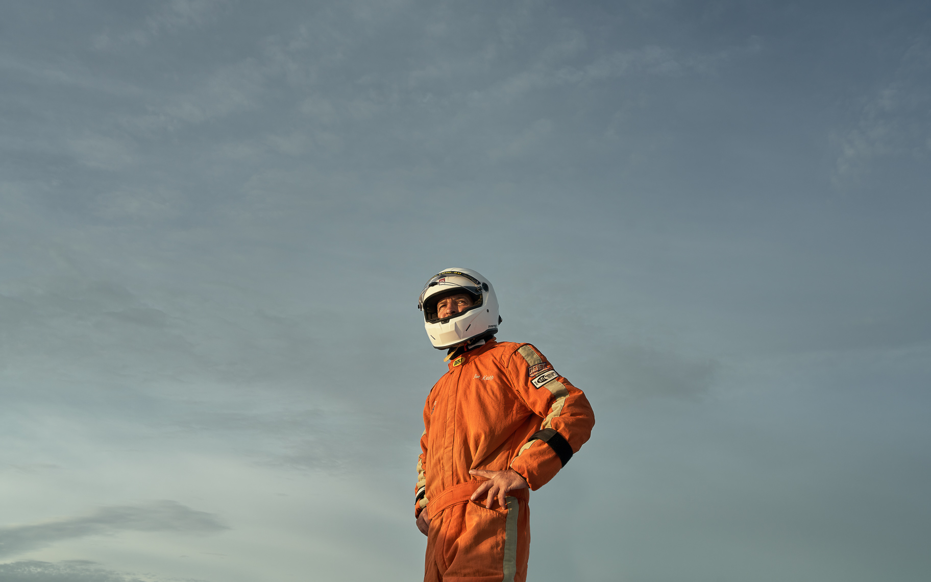 A person in an orange race suit looks into the distance